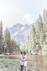 Couple kissing in front of lake with trees and mountains in background in Yosemite California